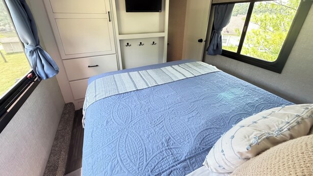 A bedroom with a bed, a television, a wardrobe, and a window with curtains.