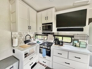A compact kitchen with white cabinets, a microwave, a stove, and a window with a view.