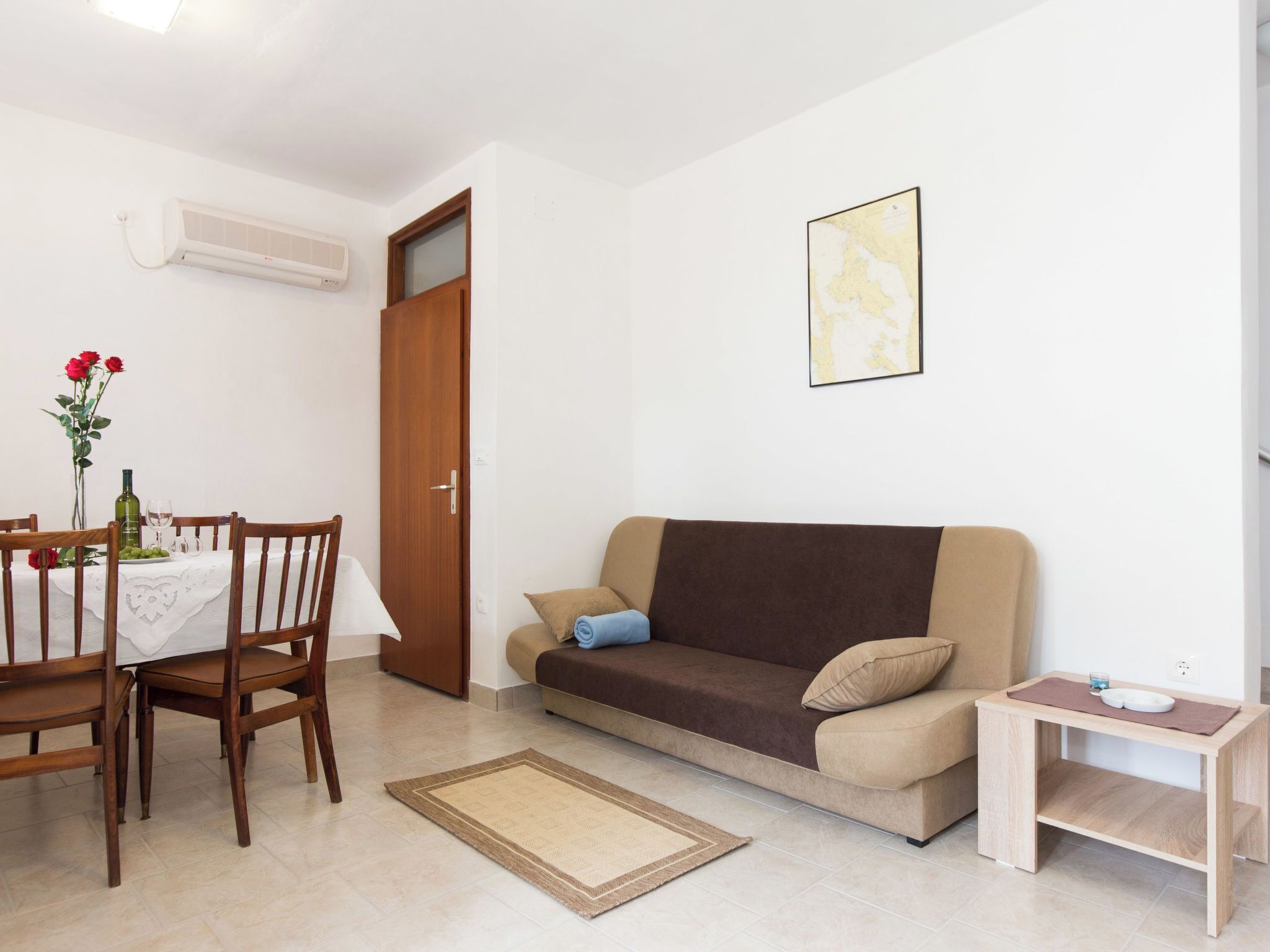A living room with a sofa, a dining table with chairs, a small wooden side table, and a rug.