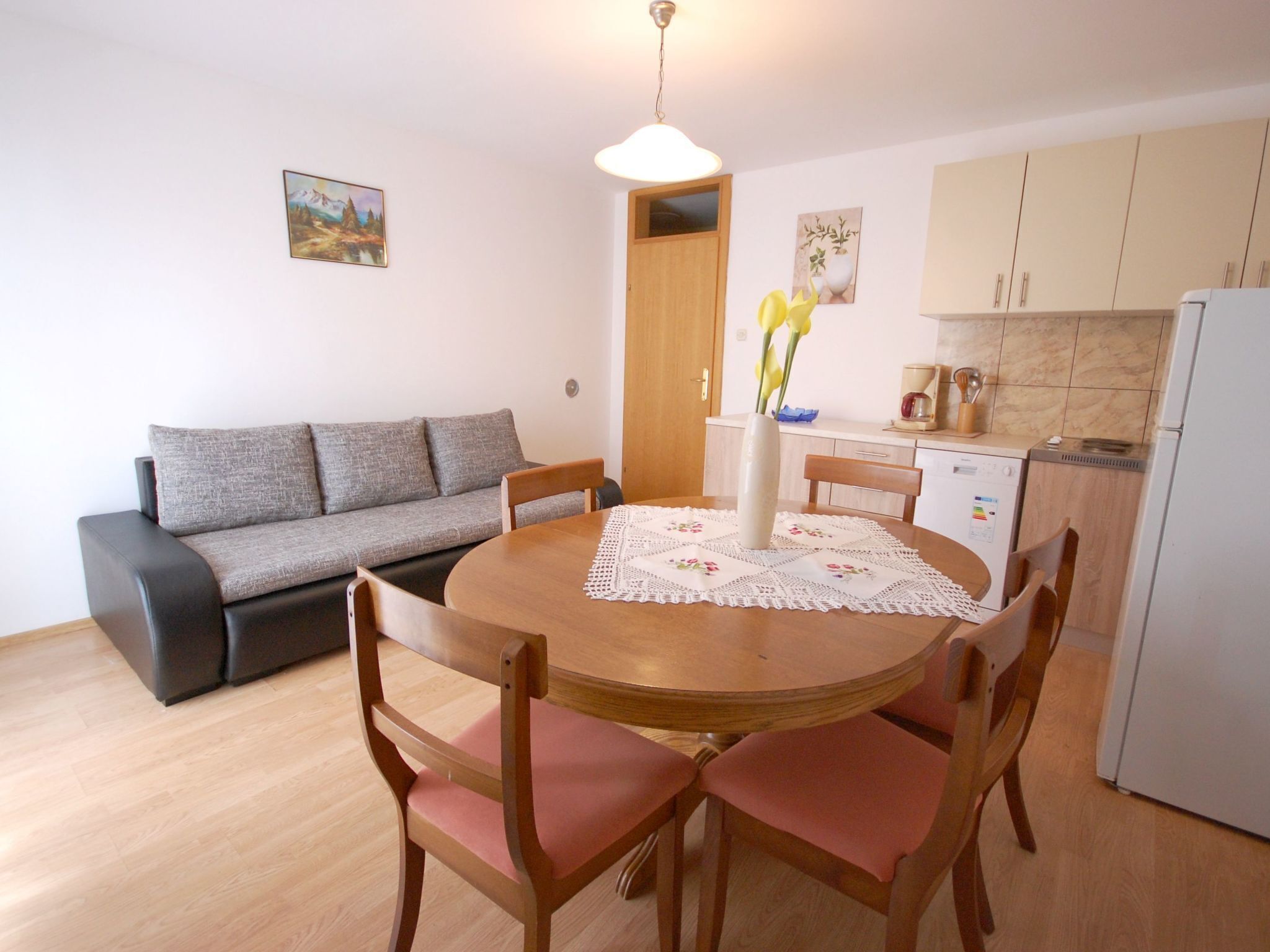 A compact living space with a dining table, chairs, a sofa, a kitchen area, and a door leading to another room.