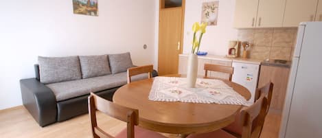 A compact living space with a dining table, chairs, a sofa, a kitchen area, and a door leading to another room.
