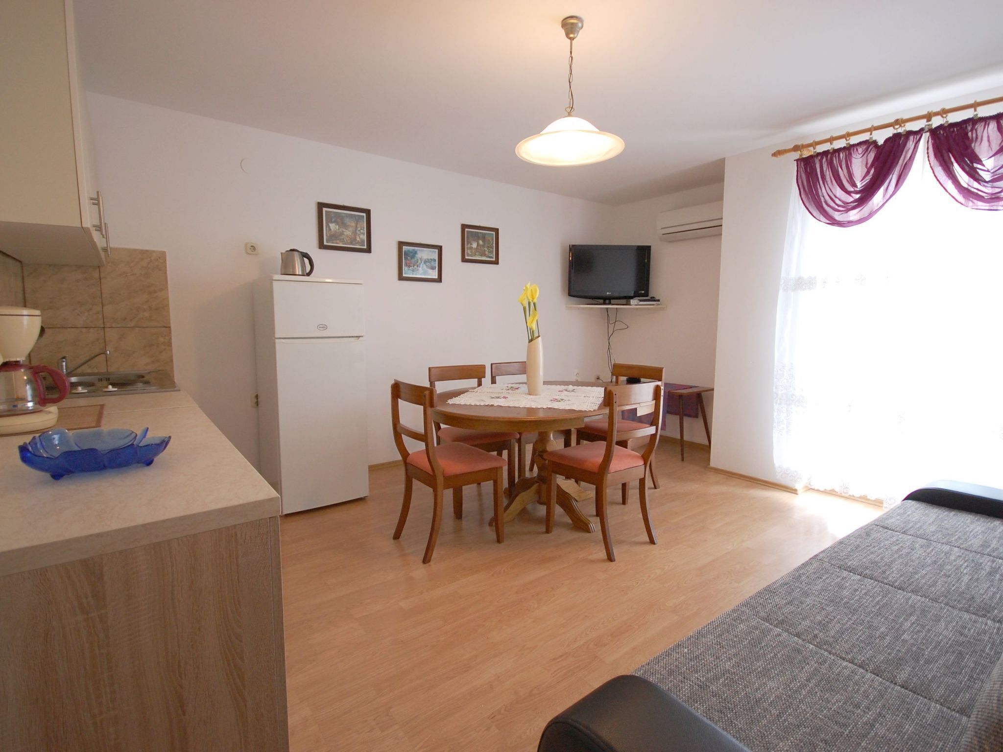 A compact living space with a kitchenette, a dining area with a table and chairs, a television, and a sofa.