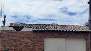 A building with a tiled roof, a brick facade, and a closed roller shutter door. - Casa de praia com 2 quartos toda mobiliada para finais de semana. (Camocim)