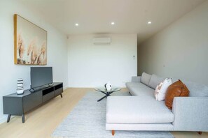 Ein modernes Wohnzimmer mit einem grauen Sofa, einem Glastisch, einem Flachbildfernseher auf einem schwarzen TV-Möbel und einem Bild an der Wand.