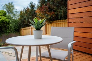 Ein runder, weißer Tisch mit einem Blumentopf, ein weißer Stuhl und ein Holzzaun im Hintergrund.