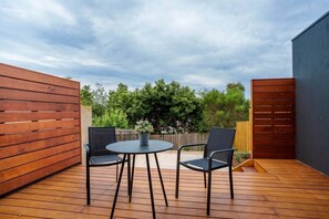 Um deck de madeira com uma mesa redonda e duas cadeiras, cercado por cercas de madeira e vegetação.