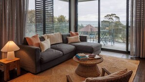 A modern living room with a sectional sofa, a round coffee table, a wicker chair, and a lamp. - Ocean-View Apartment in Heart of Portarlington (Portarlington)