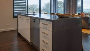 A modern kitchen with a large island, white cabinetry, and a view through the windows. - Ocean-View Apartment in Heart of Portarlington (Portarlington)