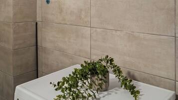 Un baño con una lavadora blanca, un perchero negro y una planta en maceta.