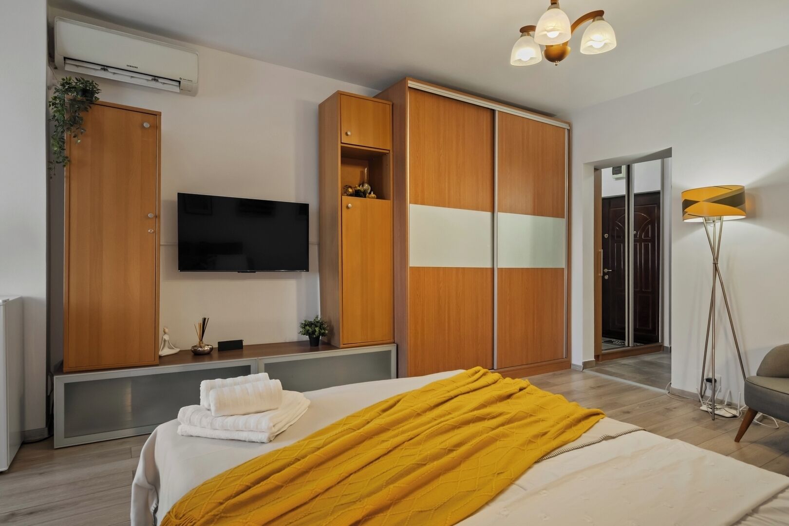 Ein modernes Hotelzimmer mit Bett, Fernseher, Kleiderschrank und Stehlampe.