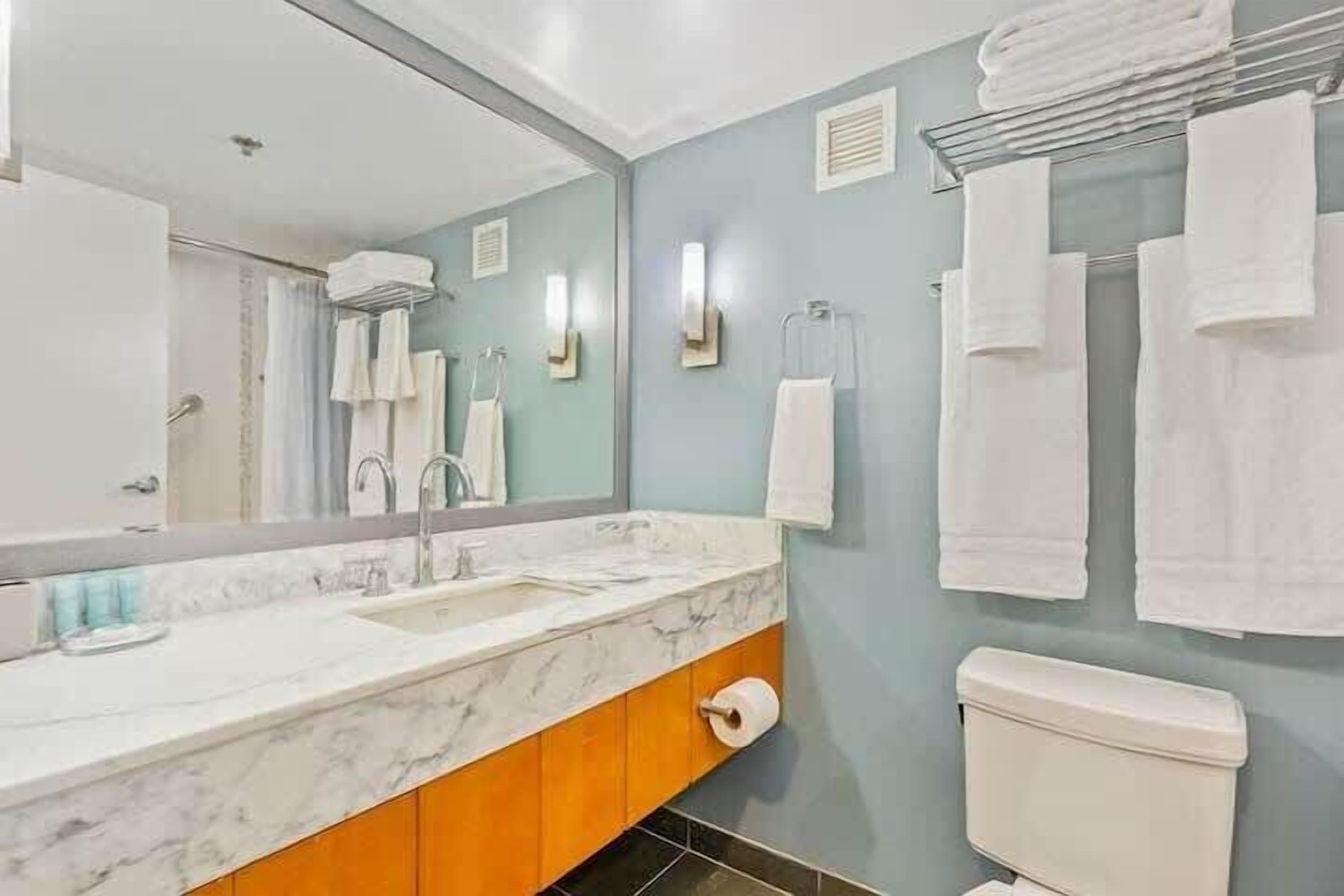 A bathroom with a marble sink, wooden cabinets, a toilet, and towels hanging on a rack.