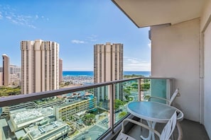 Un balcón con mesa y sillas, con vista a un paisaje urbano con edificios altos y al mar.