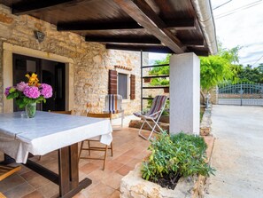 A stone building with a covered patio, a table with a white tablecloth, two chairs, a potted plant, and a metal gate. - Villa Casa San Pietro by Interhome (Pula/Banjole)