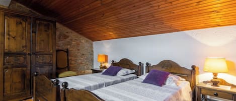 A bedroom with two wooden beds, stone walls, and wooden ceiling beams.