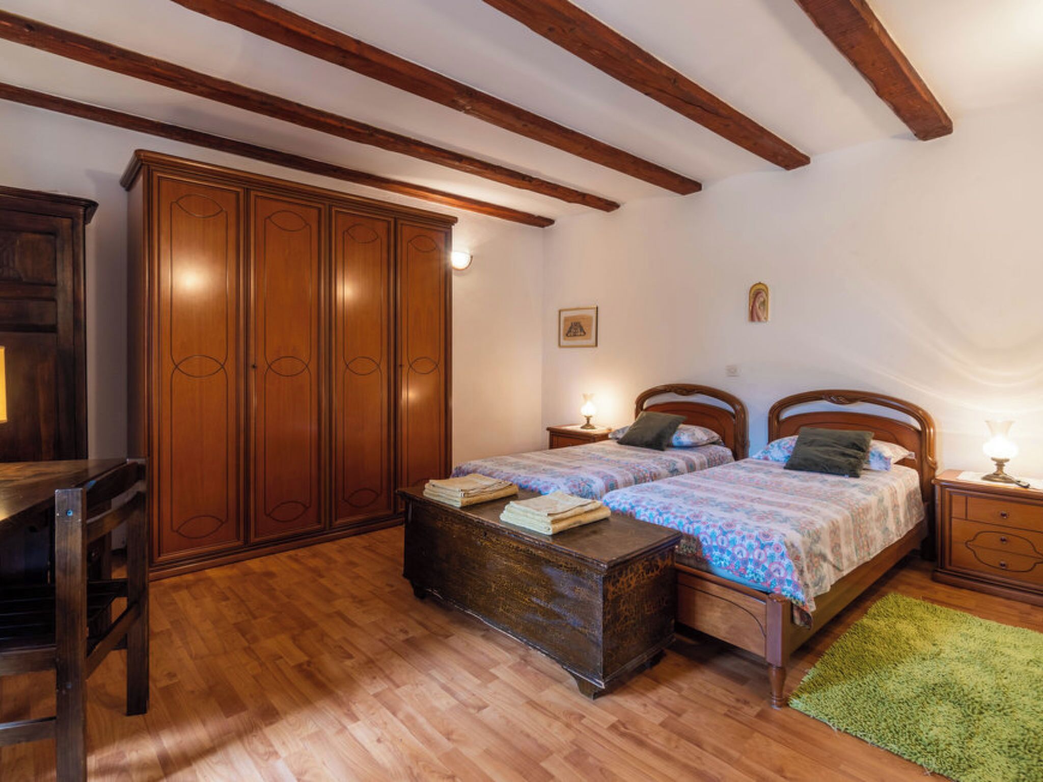 A bedroom with two wooden beds, a wardrobe, a desk, and a green rug.