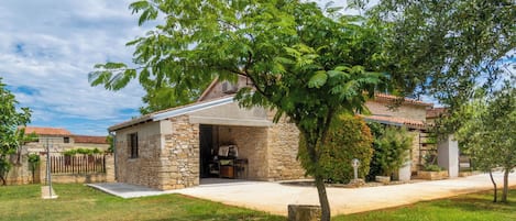 Uma casa de pedra com varanda coberta, cercada por um gramado e árvores.