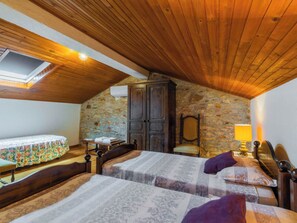 Une chambre mansardée chaleureuse avec un plafond en bois incliné, un mur en pierre, un lit recouvert d’une courtepointe à motifs, une armoire en bois et une petite table avec une lampe.