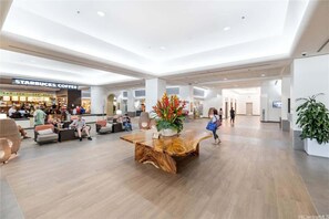 A spacious lobby with a Starbucks coffee shop, a large wooden coffee table, and seating areas. - Ala Moana Condo w_Amazing Views 1122 (Honolulu)