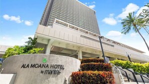 En høj bygning, der huser et hotel med moderne design, et skilt der viser, at det er Ala Moana Hotel by Marriott, og en klar himmel.