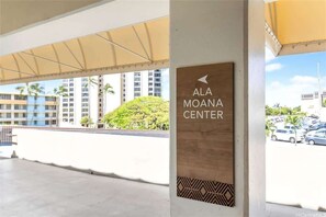 Schild für das Ala Moana Center mit Blick auf hohe Gebäude und parkende Autos.
