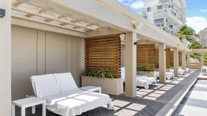 A sunlit outdoor seating area with white lounge chairs and tables, wooden slats, and potted plants. - Beautiful Studio at Ala Moana 1330 HONOLULU (Honolulu)