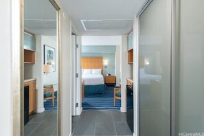 A hotel room with a bed, bedside table, chair, and a desk with a lamp. - Stunning Ala Moana 1BR W| Balcony & Mountain/City Views (Honolulu)