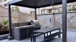 An outdoor kitchen area with a grill, a sink, and a table with benches. - Serviced Studio in Santiago in Greystar Somma (Santiago)