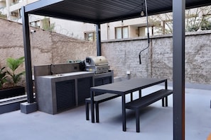 Uma área de cozinha externa com churrasqueira, pia e mesa com bancos.