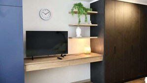 A modern living room with a flat-screen TV, a clock, a shelf with a plant, and a cabinet. - Serviced Studio in Santiago in Greystar Somma (Santiago)