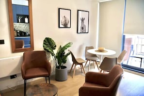 Uma sala de estar moderna com uma poltrona de couro marrom, uma mesa de centro redonda, uma planta em vaso e uma área de jantar com uma mesa e cadeiras brancas.