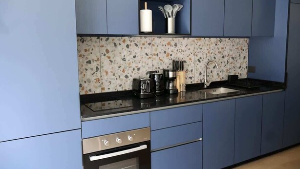 A modern kitchen with blue cabinets, a speckled backsplash, and stainless steel appliances. - Serviced Studio in Santiago in Greystar Somma (Santiago)
