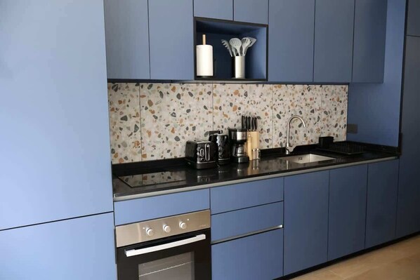 A modern kitchen with blue cabinets, a speckled backsplash, and stainless steel appliances.