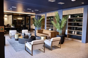 Um lobby moderno com sofá, cadeiras, mesa de centro e plantas em vasos.