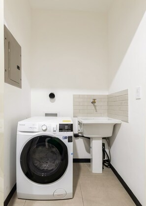 Ein kleiner Waschraum mit einer Waschmaschine mit Frontlader, einem Waschbecken und einer gefliesten Rückwand.