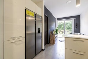Eine moderne Küche mit Edelstahlgeräten, einer dunklen Wand und einem Fenster mit Blick auf Grünflächen.