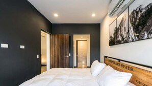 Ett hotellrum med en stor säng, en sänggavel i trä, en väggmonterad luftkonditioneringsanläggning och en inramad tavla med ett bergsmotiv.
