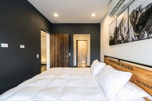 Ein Hotelzimmer mit einem großen Bett, einem hölzernen Kopfteil, einer Wandklimaanlage und einem Bild von Bergen im Rahmen.