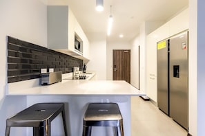 Cocina moderna con encimera blanca, salpicadero negro, electrodomésticos de acero inoxidable y dos taburetes negros.
