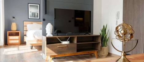 A modern hotel room with a large flat-screen TV, wooden furniture, a bed with white linens, and a decorative floor lamp.