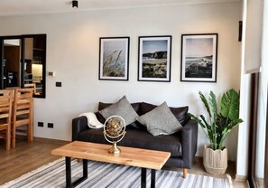 A modern living room with a black leather sofa, a wooden coffee table, and three framed landscape pictures on the wall. - Corporate 1 Bedroom in Santiago in Somma Asturias (Las Condes)