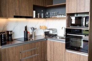 A modern kitchen with wooden cabinets, a built-in microwave, a coffee maker, and a fish decoration. - Corporate 1 Bedroom in Santiago in Somma Asturias (Las Condes)
