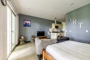 A modern bedroom with a large bed, a TV, a desk, and a kitchenette. - Furnished Studio in San Jose Urban Flats Building (Pozos)