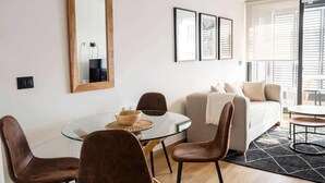 Ein modernes Wohnzimmer mit einem Glastisch, braunen Ledersesseln, einer Couch und einem großen Fenster mit Jalousien.