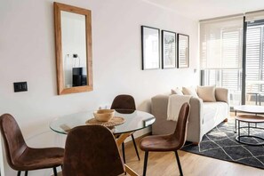 Ein modernes Wohnzimmer mit einem Glastisch, braunen Ledersesseln, einer Couch und einem großen Fenster mit Jalousien.