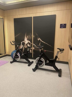 Dos bicicletas estáticas en una habitación con un panel de pared de madera y un espejo grande.
