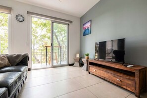 Ein Wohnzimmer mit einer Couch, einem Fernseher auf einem Holzboden, einer Schiebetür aus Glas und einem Gemälde an der Wand.