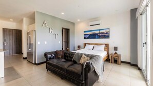 A modern bedroom with a bed, a leather sofa, a painting, and a kitchenette. - Corporate Studio in San Jose Urban Flats Building (Pozos)