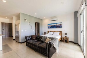 A modern bedroom with a bed, a leather sofa, a painting, and a kitchenette. - Corporate Studio in San Jose Urban Flats Building (Pozos)