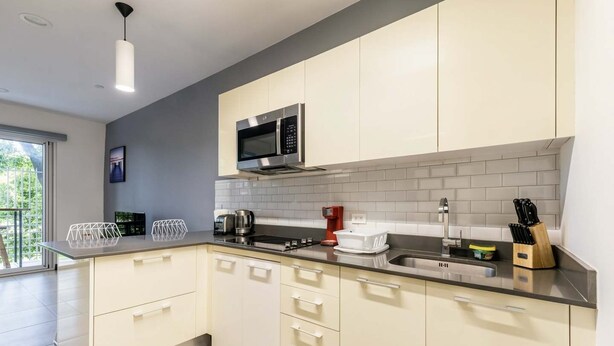 A modern kitchen with white cabinets, a stainless steel microwave, and a black countertop. - Corporate Studio in San Jose Urban Flats Building (Pozos)