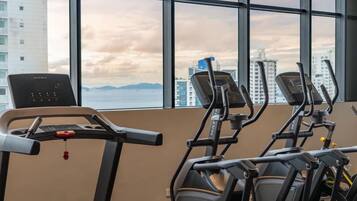 Ein Fitnessraum mit Laufbändern und Crosstrainer, große Fenster mit Blick auf die Stadt.